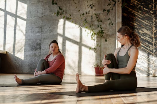 Two women in a peaceful yoga session indoors, focusing on stretching and relaxation on a sunny day.