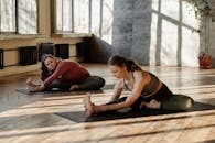 在阳光明媚的室内工作室里，两名女士正专注于健康，在瑜伽垫上伸展身体