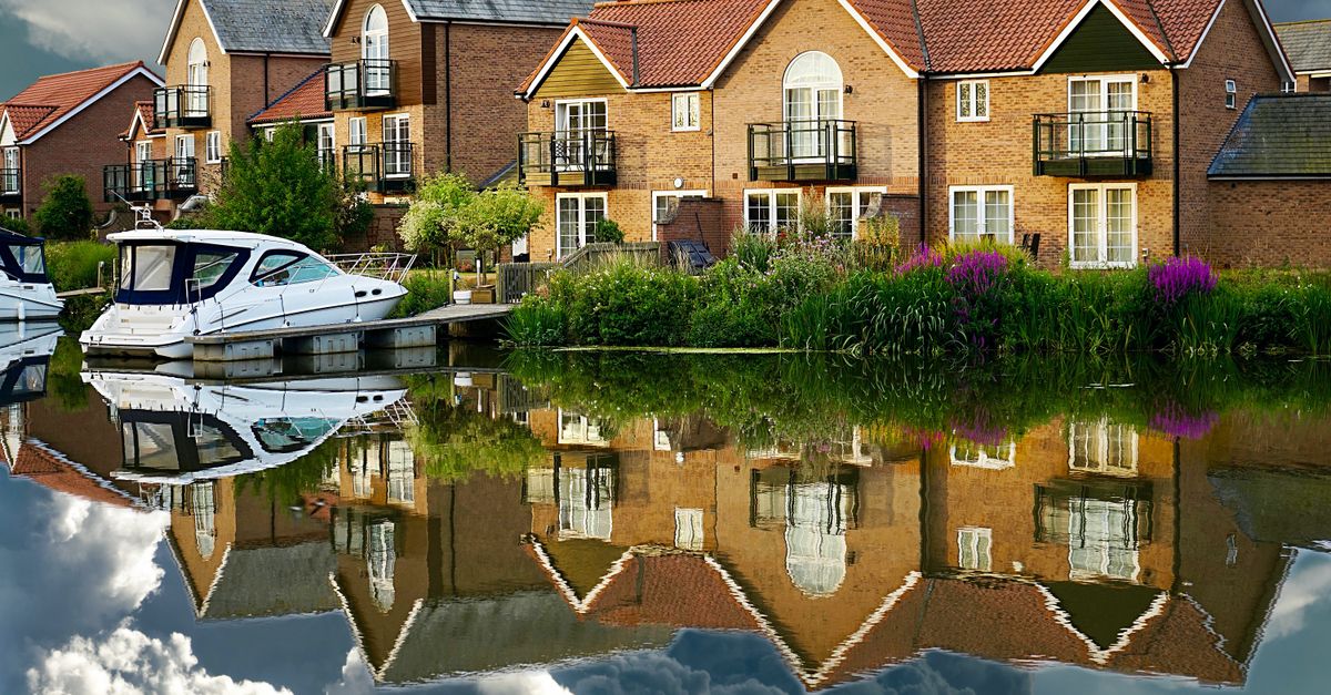 Picturesque houses and yachts reflected on a serene canal under dramatic skies.