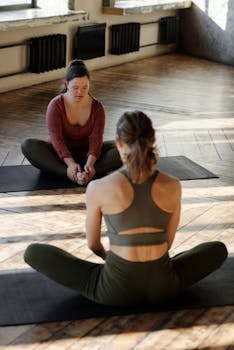 Two women practicing yoga in a sunlit studio, focusing on flexibility and relaxation.