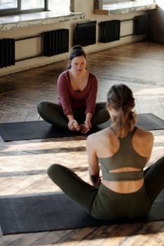 Two women practicing yoga together in a sunlit studio, promoting wellness and inclusivity.
