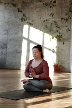 Young woman with Down syndrome practicing yoga in a sunlit indoor space, promoting wellness.