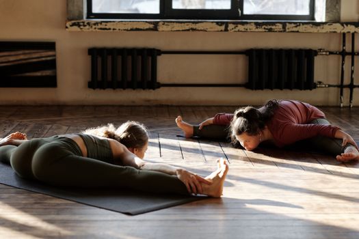 Two women performing yoga splits indoors, focusing on flexibility and relaxation.