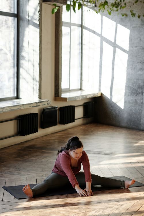Free A woman with down syndrome practicing a yoga stretch indoors in natural daylight. Embracing fitness and wellness. Stock Photo
