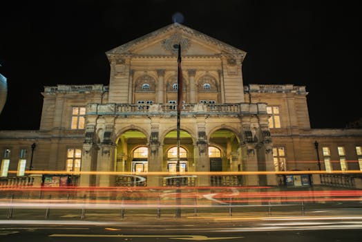 Dramatic long exposure of a historic theater building at night with light trails in the foreground.