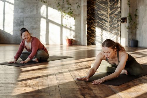 Free Two women practicing yoga indoors, stretching on mats in natural light. Stock Photo