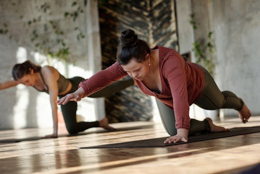 Two women focused on a yoga pose indoors, promoting balance and wellness.