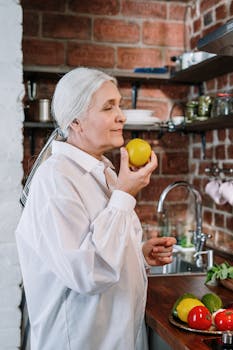 A senior woman with grey hair enjoys the aroma of a fresh lemon in a rustic kitchen.
