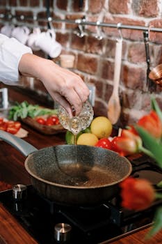 A close-up of home cooking with fresh ingredients being added to a pan in a cozy kitchen setting.