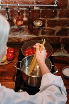A close-up of a person cooking spaghetti in a rustic kitchen, set against a brick wall.