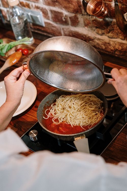 Free A person prepares spaghetti with tomato sauce in a cozy kitchen setting. Stock Photo