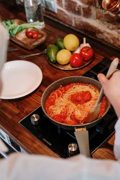 Free A person cooking spaghetti with tomato sauce in a cozy kitchen, showcasing fresh ingredients. Stock Photo