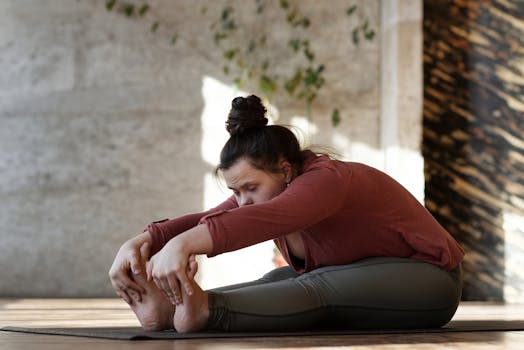 A woman sitting indoors on a yoga mat in a calm and relaxed pose, emphasizing fitness and wellness.