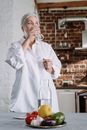 一位优雅的女士在舒适的厨房里喝水，桌上摆着新鲜的蔬菜