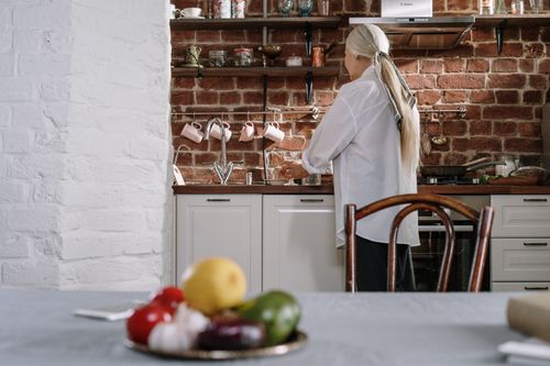 Free Senior woman cooking in a cozy kitchen with fresh vegetables on the table. Stock Photo