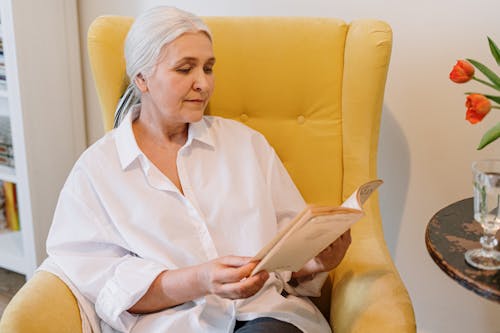 Free An Elderly Woman Sitting On A Couch Reading A Book Stock Photo