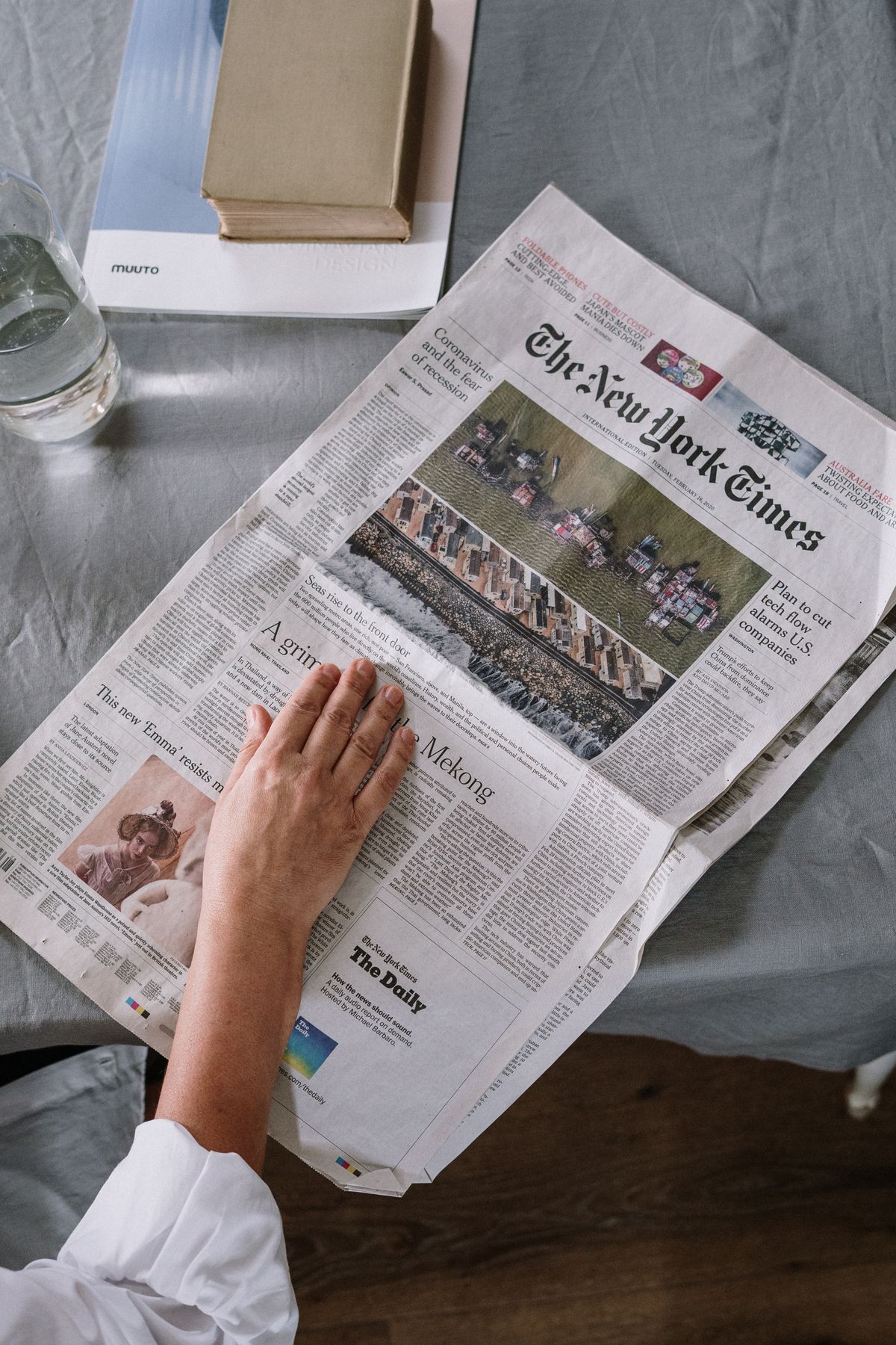 A person reading a printed newspaper at a table