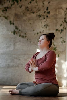 A young woman with Down syndrome focuses on inner peace while practicing yoga indoors.