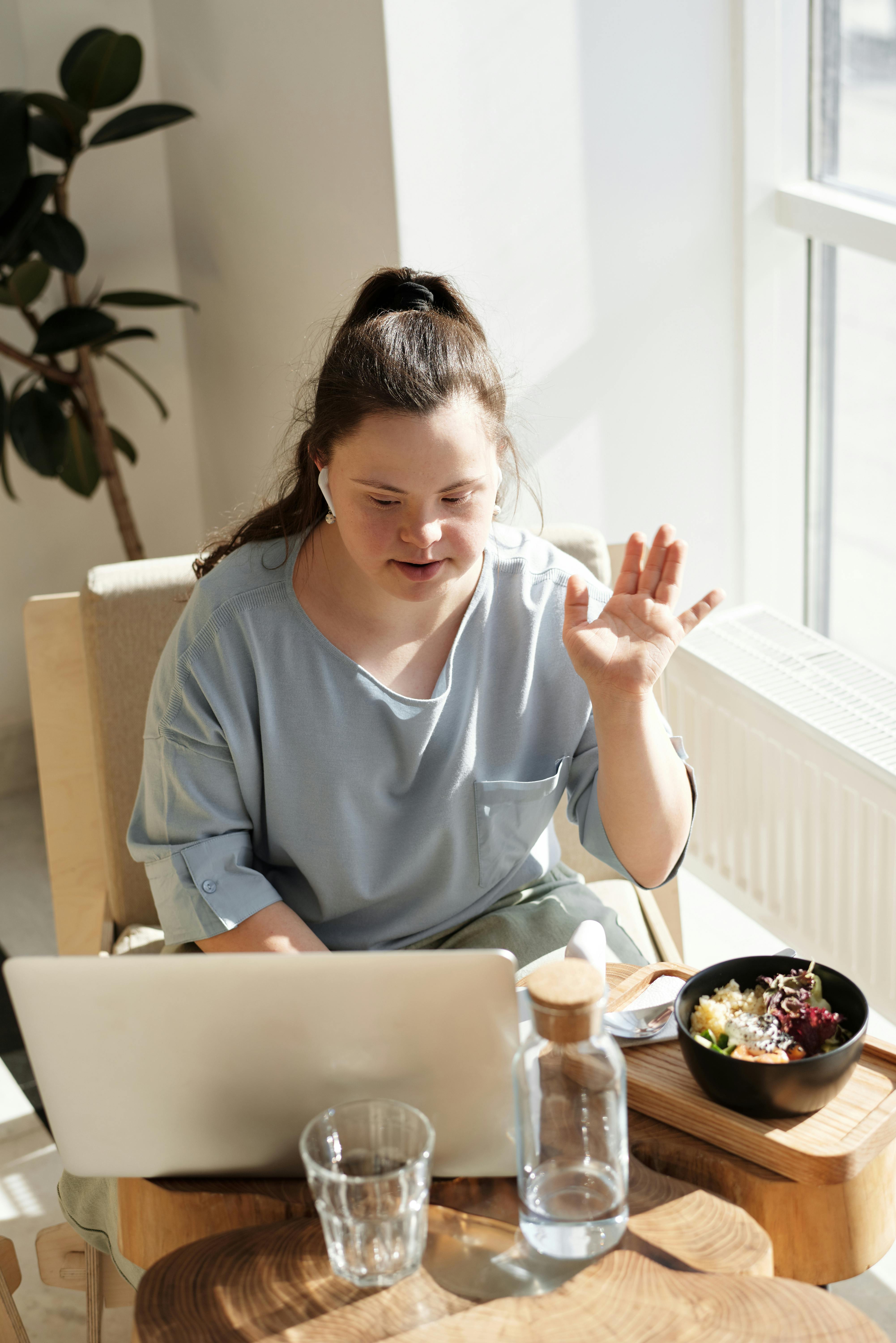 woman in a blue top using a laptop near a glass window