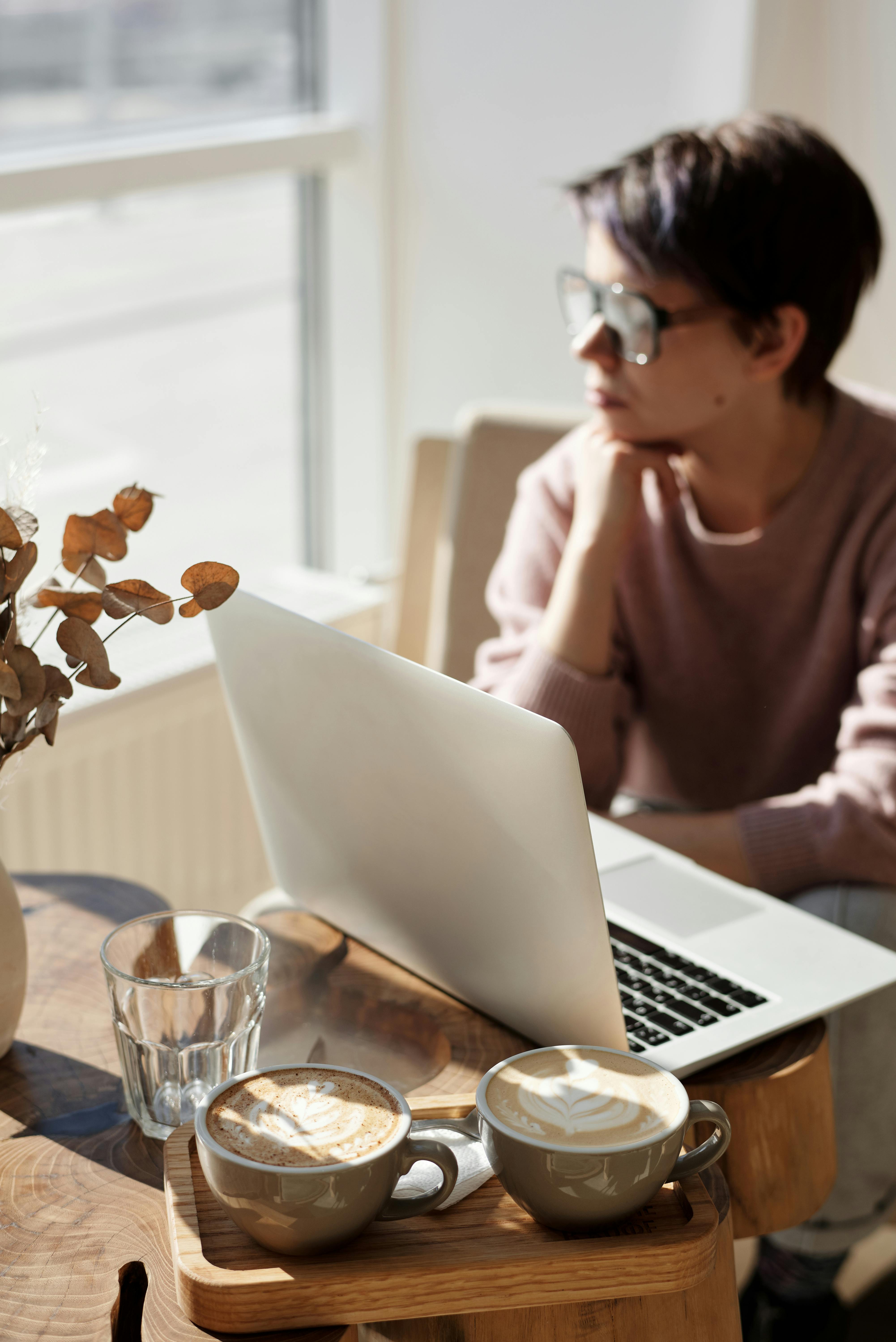 一名女子坐在窗边，喝着咖啡，用笔记本电脑工作