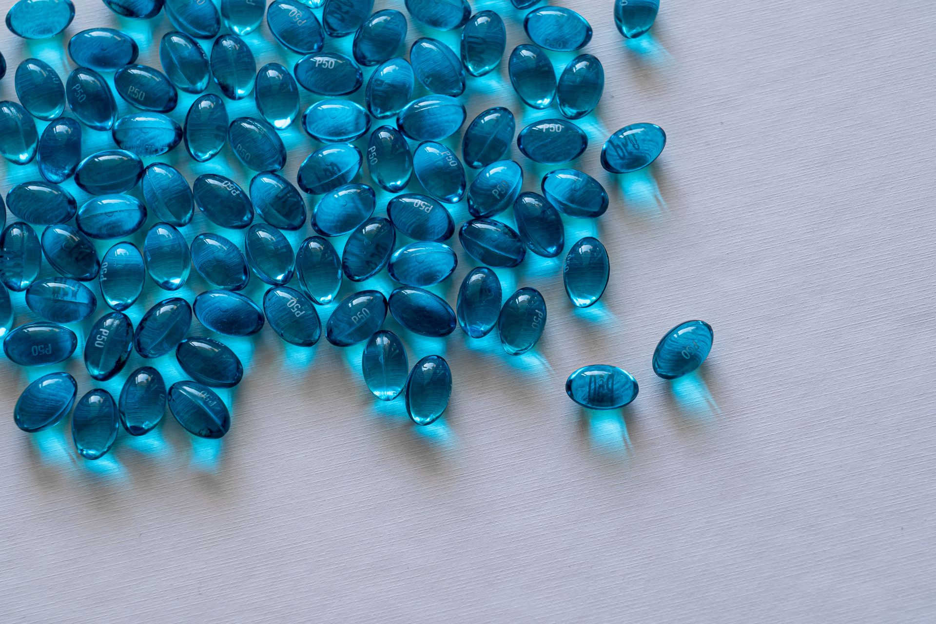 A close-up view of scattered blue gel capsules on a white surface, showcasing their glossy texture.