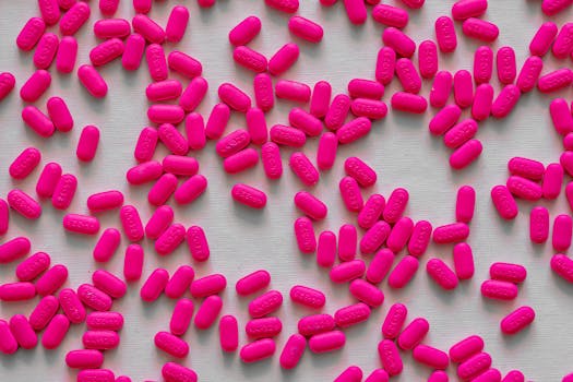 A close-up image of neon pink pills scattered across a light surface, showcasing their vibrant color and form.