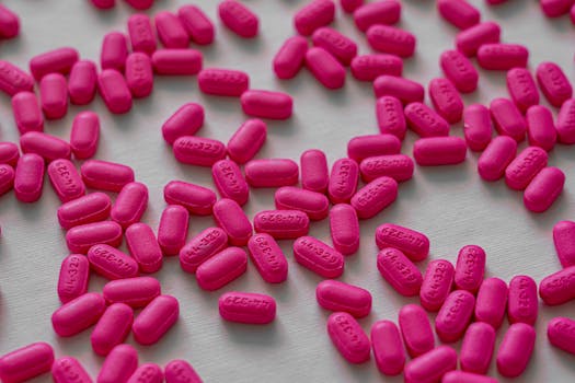 Close-up view of pink tablets scattered on a white table for medication and health treatment.