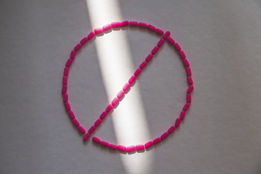 Pink pills arranged in a prohibition symbol in sunlight, symbolizing drug restrictions.