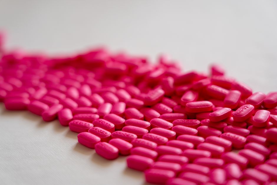 A close-up shot of scattered neon pink pills on a white surface.