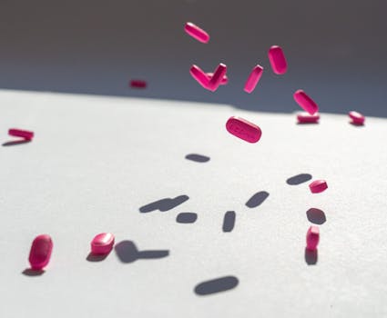 Pink pills suspended in air casting shadows on a white background.