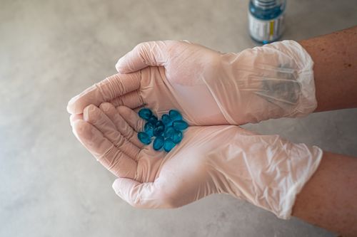 Free Close-up of gloved hands holding blue capsules, representing healthcare and medication. Stock Photo