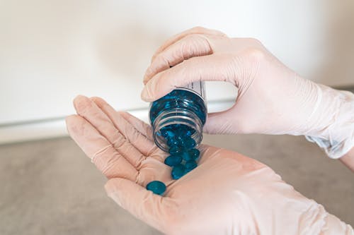 Free Person Holding Plastic Bottle with Blue Pills Stock Photo