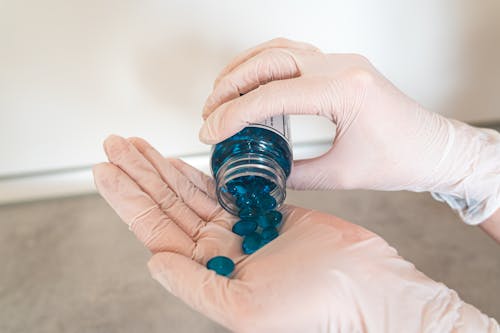 Person Holding Plastic Bottle with Blue Pills