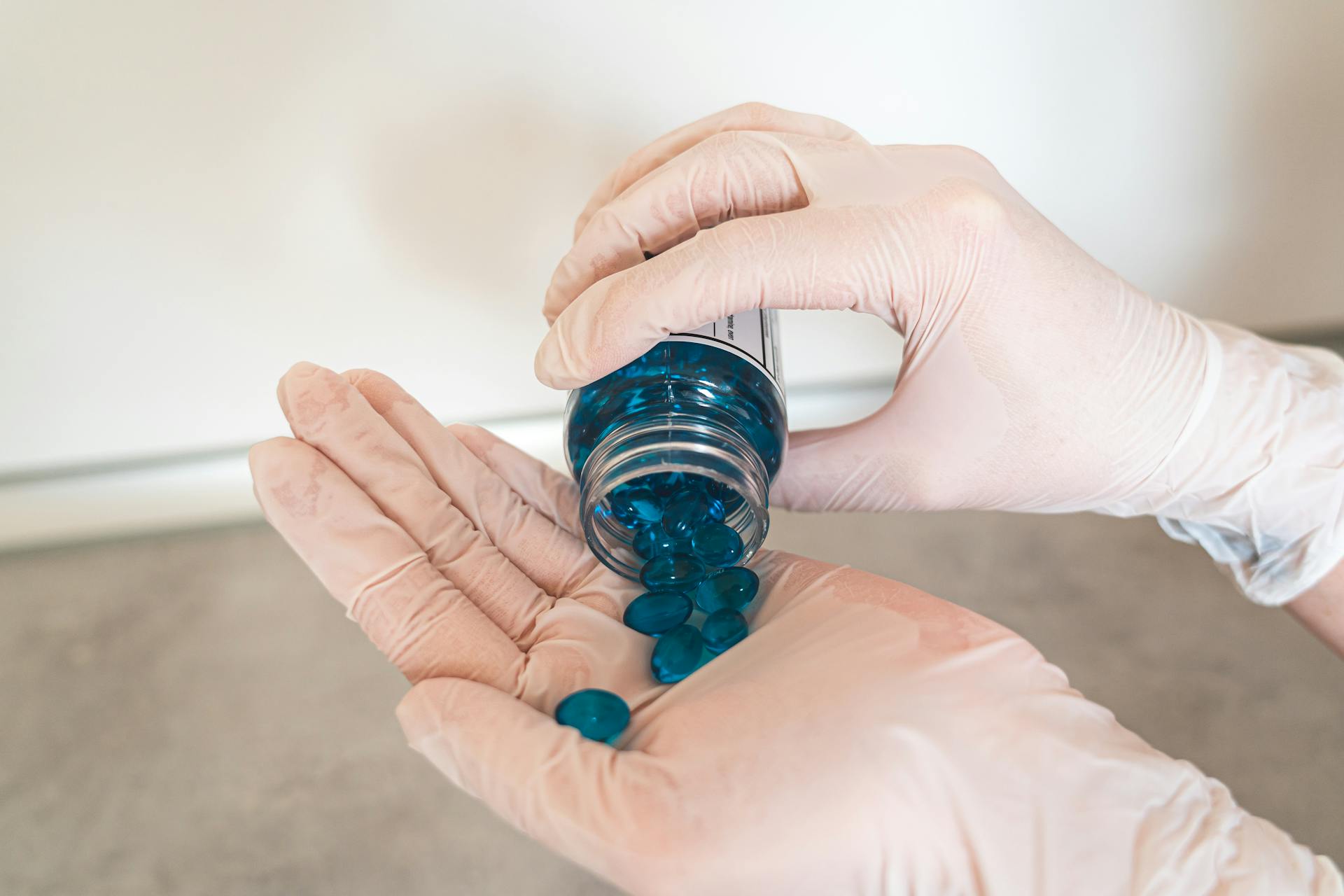 Close-up of hands in gloves pouring blue pills from a bottle, symbolizing medication and healthcare.