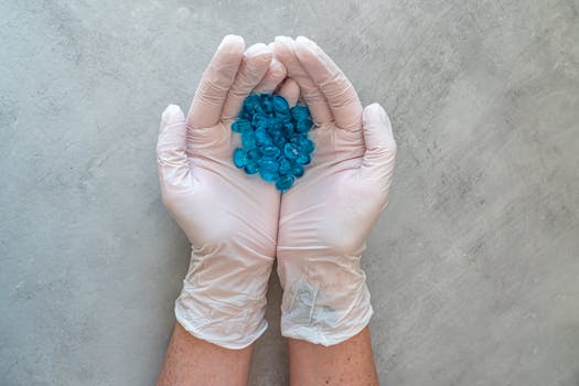 Close-up of hands in latex gloves holding blue capsules on a grey background.