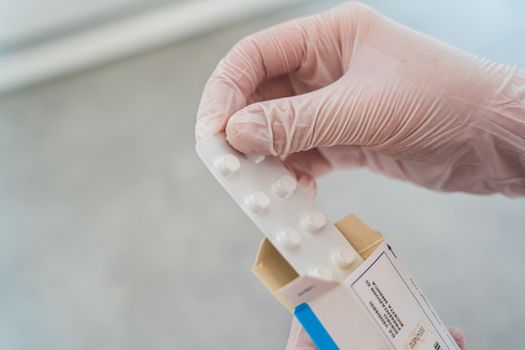 Close-up of a hand in gloves holding a blister pack of pills, symbolizing medical care.