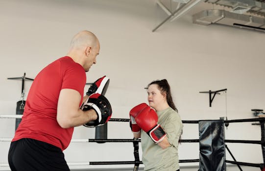 A personal trainer guides a young woman with Down syndrome during a boxing session indoors.