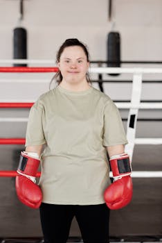 Woman with Down syndrome confidently posing in boxing gloves inside a modern gym.