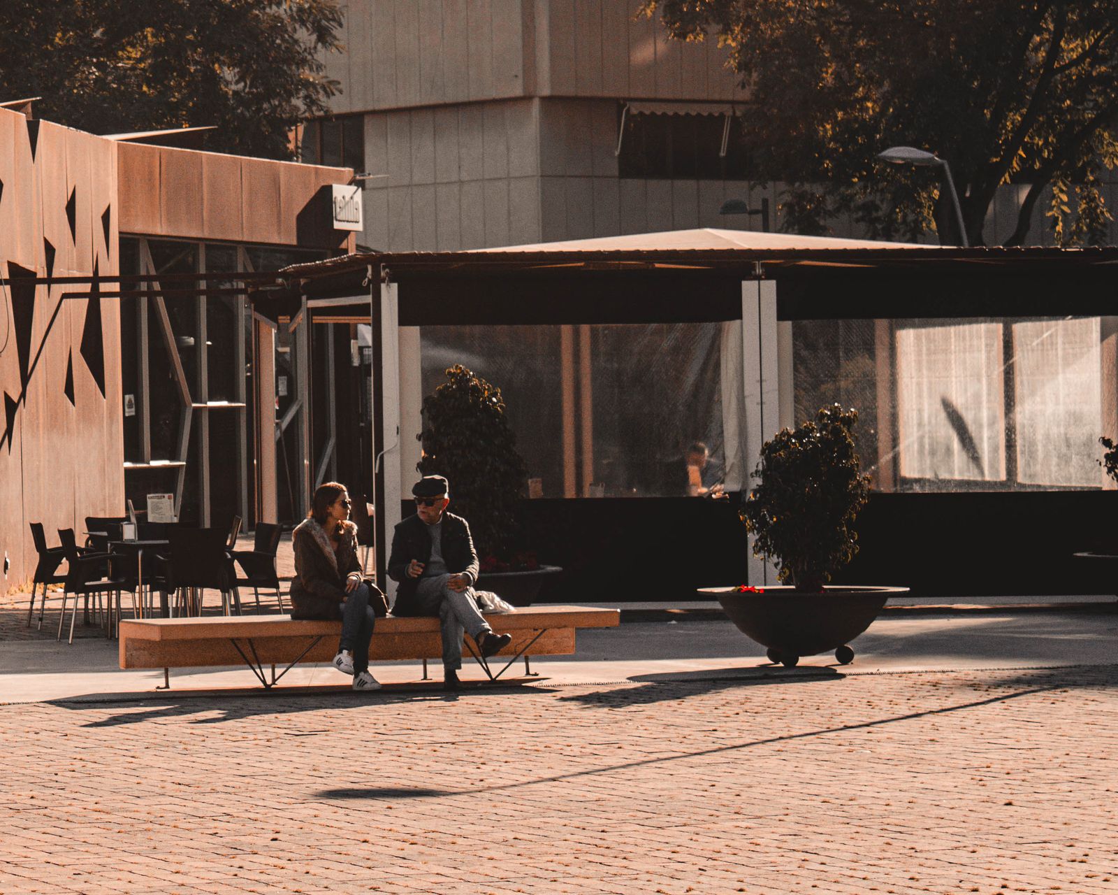 Two people talking while sitting on a bench outside a café