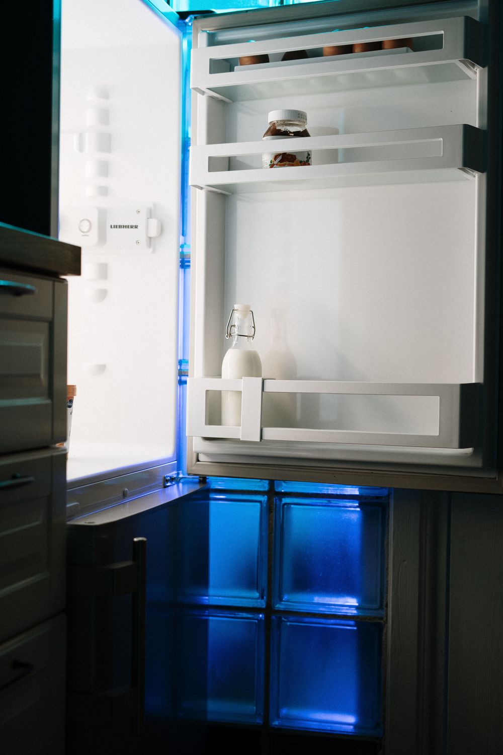 Open refrigerator with minimal contents illuminated by interior light in a home kitchen