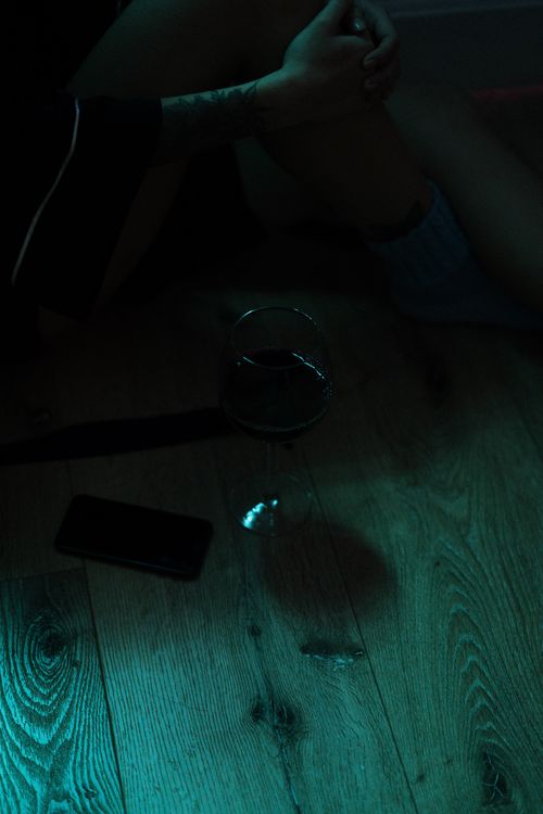 Free A dimly lit cozy home scene featuring a wine glass on a wooden floor and a person relaxing. Stock Photo