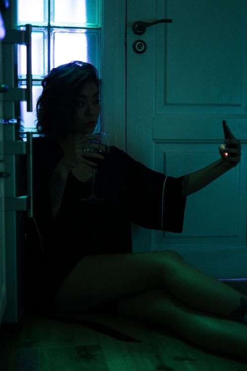 Free Asian woman enjoying a relaxed evening at home, taking a selfie with a glass of wine. Stock Photo