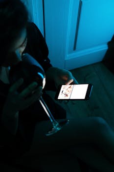 A woman enjoying wine and browsing her smartphone in a cozy, neon-lit home environment.
