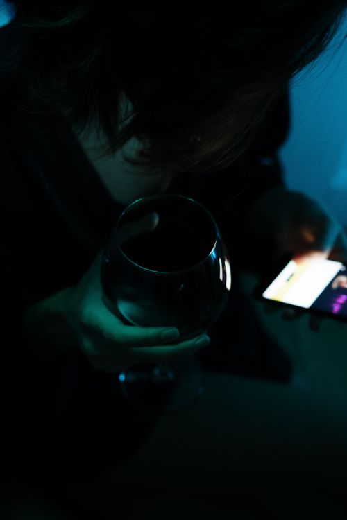 Free A person relaxes at home with a wine glass and smartphone glow at night. Stock Photo