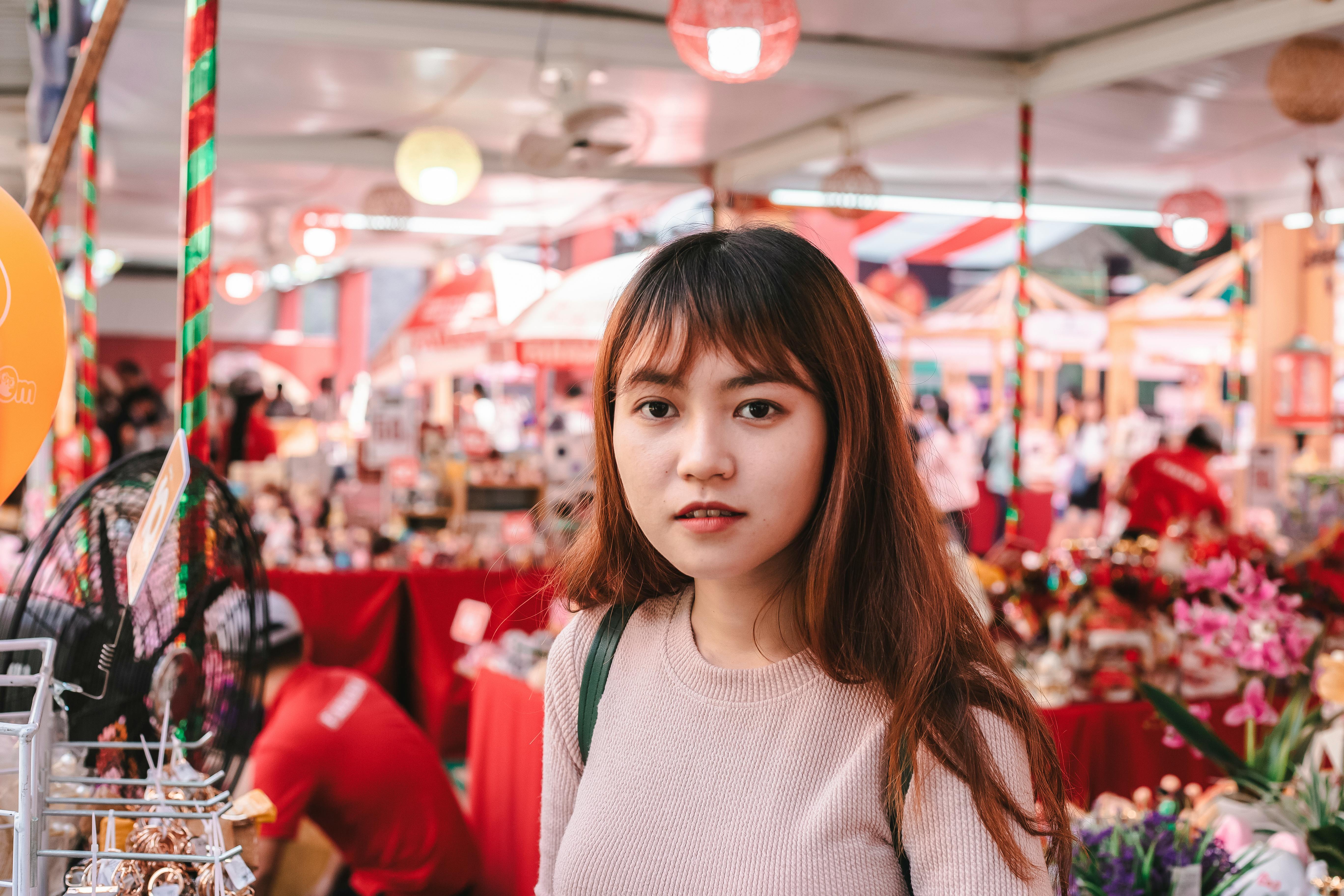 Asian woman in vibrant indoor market surrounded by colorful merchandise and shoppers.