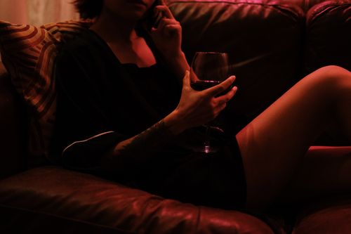 Free A relaxing evening scene with a woman on the phone, holding a glass of wine under soft lighting. Stock Photo