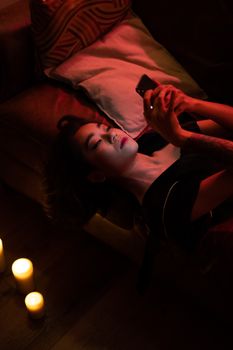Asian woman relaxing at home using smartphone by candlelight for a calming evening.