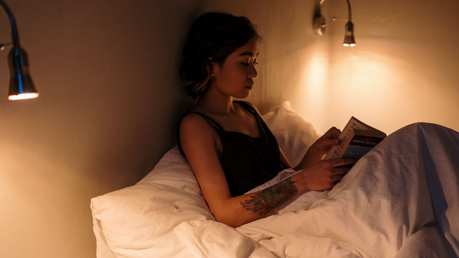 A woman reading a book in bed under warm lamp light