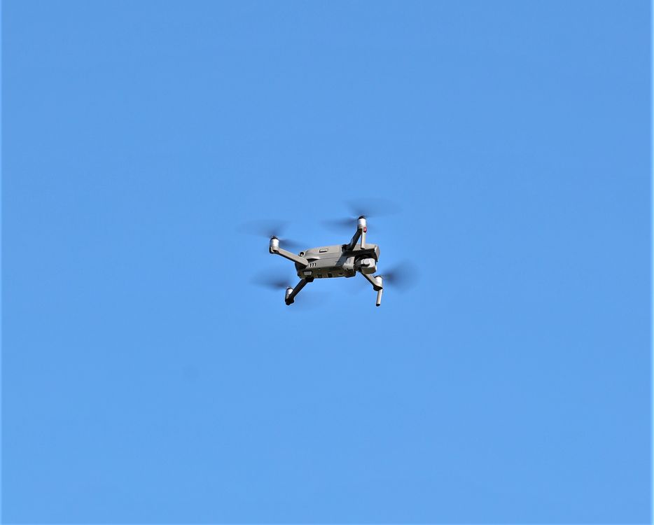 A drone in flight against a clear sky, the kind of low-altitude flight used to photograph a roof surface after a storm.