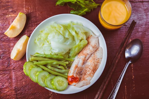 Colorful dish featuring steamed fish, veggies, cucumber, and a glass of orange juice.